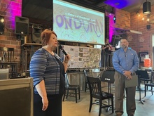 A woman speaks into a microphone while a man listens.